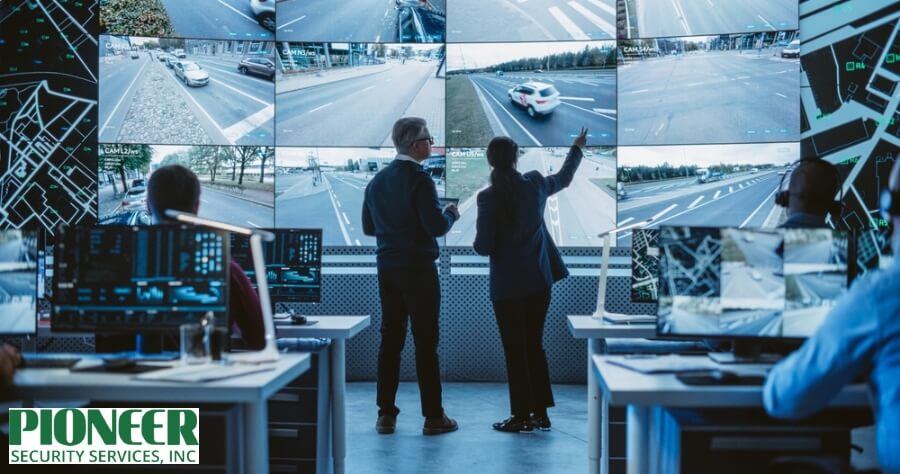 Hand operating a laptop with six screens showing home security monitoring of different residential rooms, with a coffee cup and smartphone on the desk.