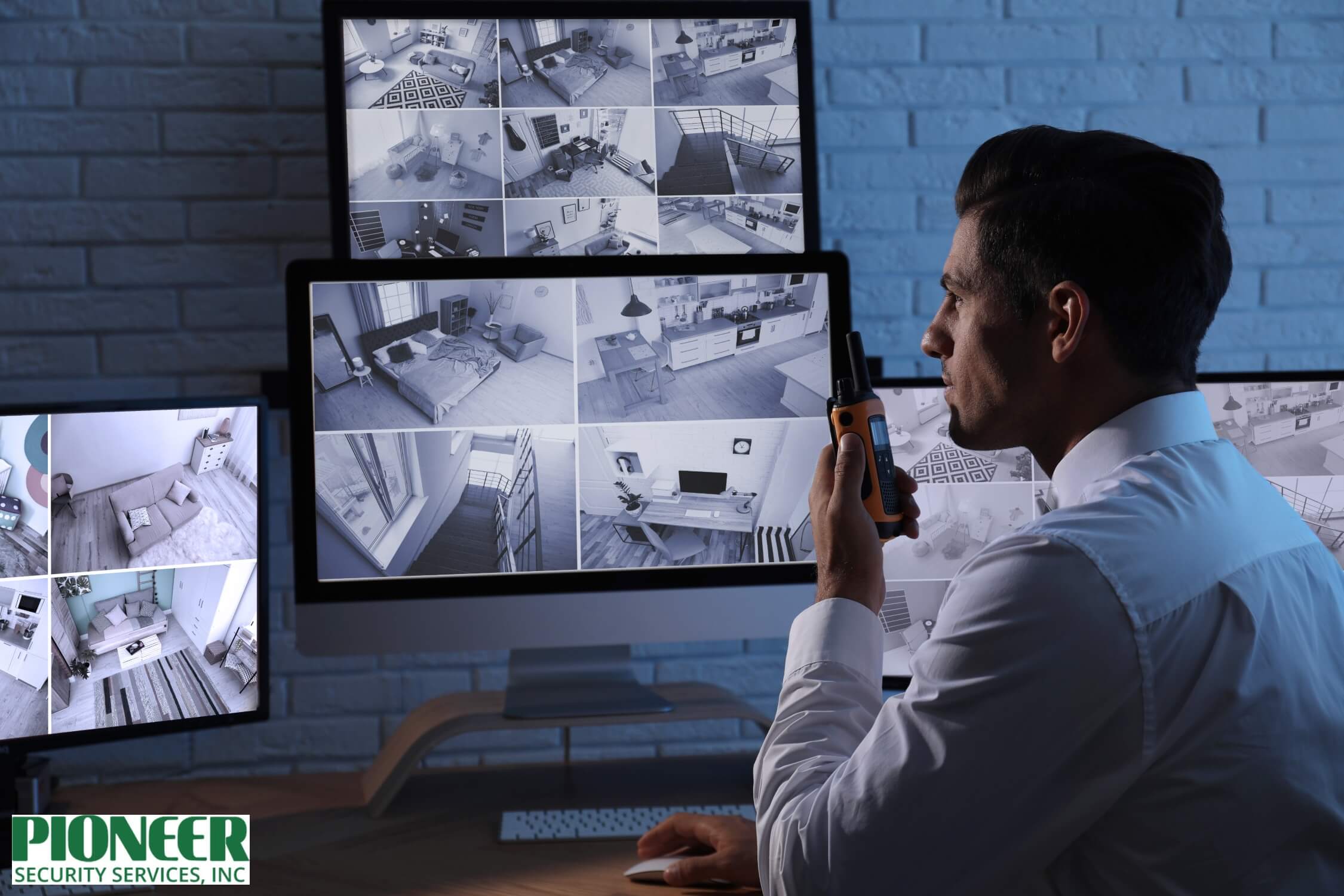 Security guard in a white shirt watching multiple live feeds from CCTV cameras on several dark-lit monitors, holding a two-way radio/walkie-talkie for communication.
